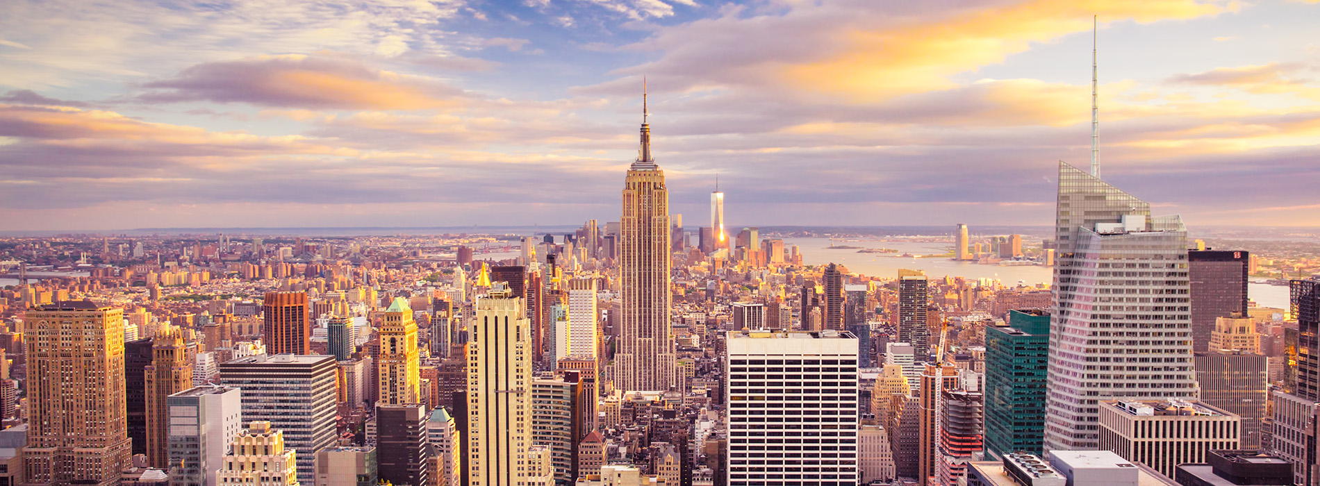 The image shows a city skyline with the Empire State Building prominently visible against a backdrop of a sunset, with clouds partially obscuring the view.