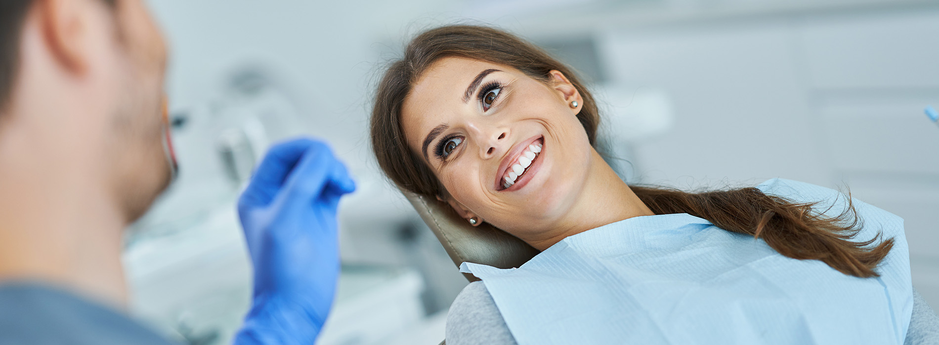 The image shows a dental professional attending to a patient during a dental appointment, with both individuals smiling at the camera.