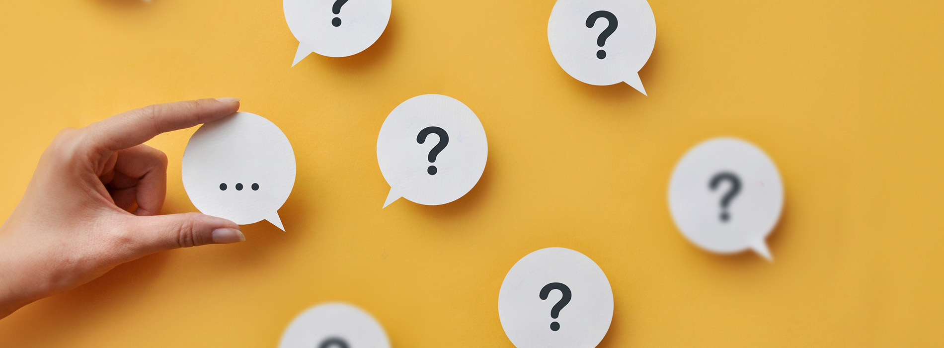 The image shows a collection of speech bubble stickers with question marks on them, attached to a yellow background, suggesting a theme of questions or inquiries.