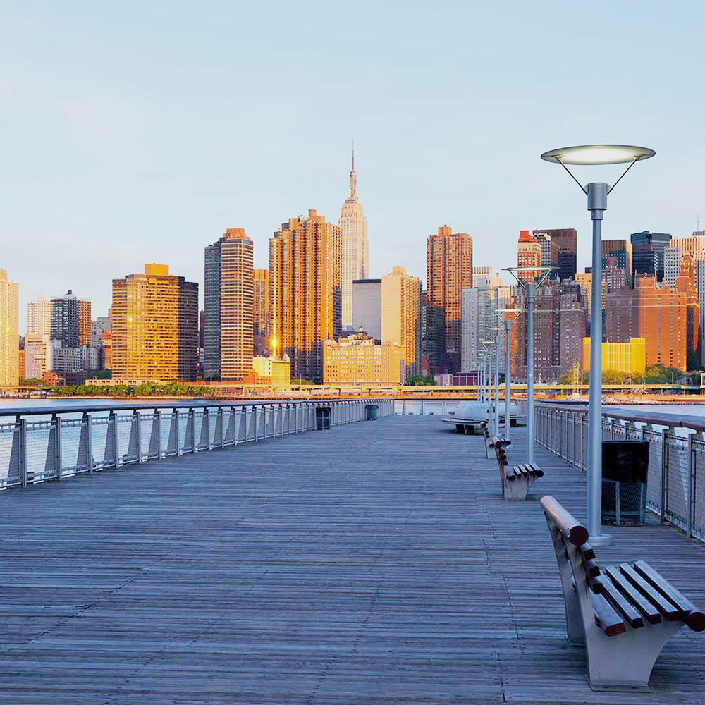 The image shows a cityscape with a skyline featuring tall buildings at dusk, viewed from a pier with benches, against a backdrop of a clear sky.