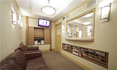 The image depicts an interior view of a waiting room with a seating area, television screen displaying static, and a reception counter with a glass partition.