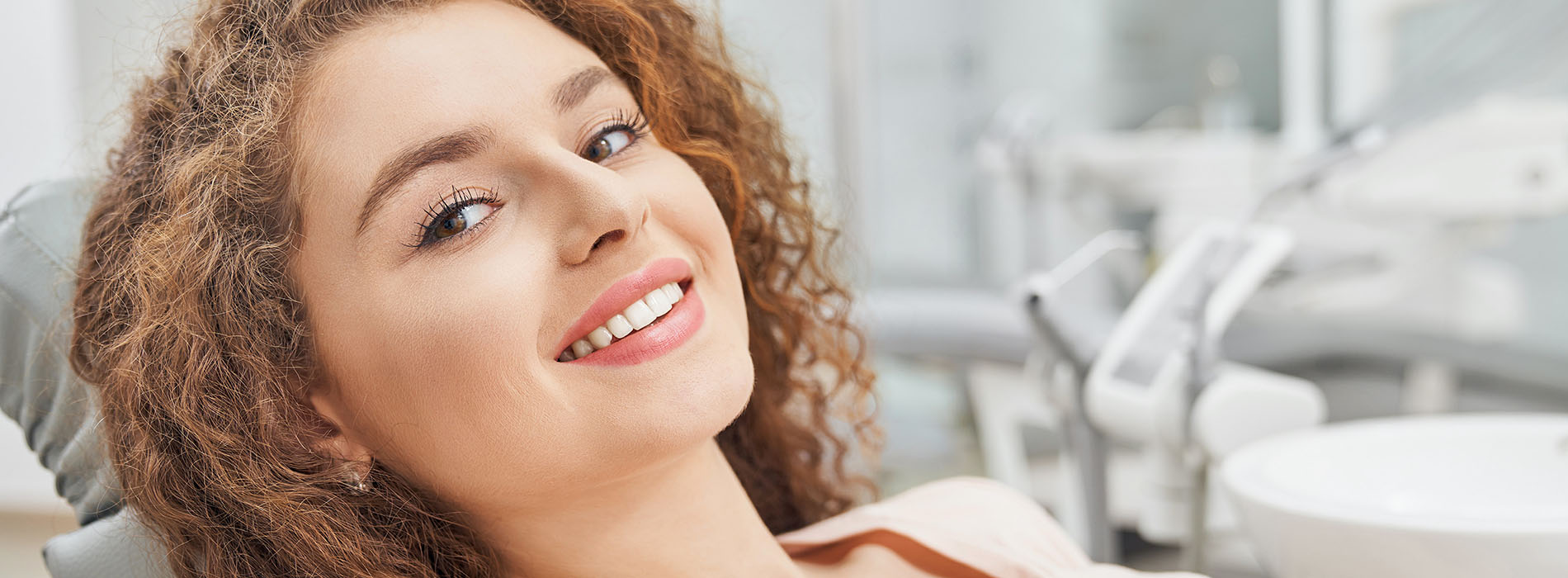 The image shows a smiling woman sitting in a dental chair, with the focus on her face and upper body.